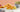 Mixed variety of crunchy snacks and a bowl of roasted green peas on a white table with peach background