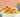 Mixed variety of crunchy snacks and a bowl of roasted green peas on a white table with peach background